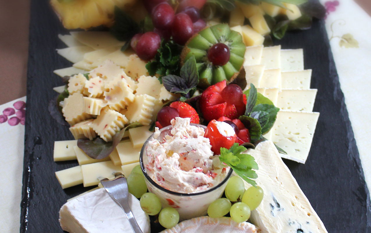 Käse-Obst-Platte mit Trauben, Erdbeeren, Kiwi und cremigem Dip.