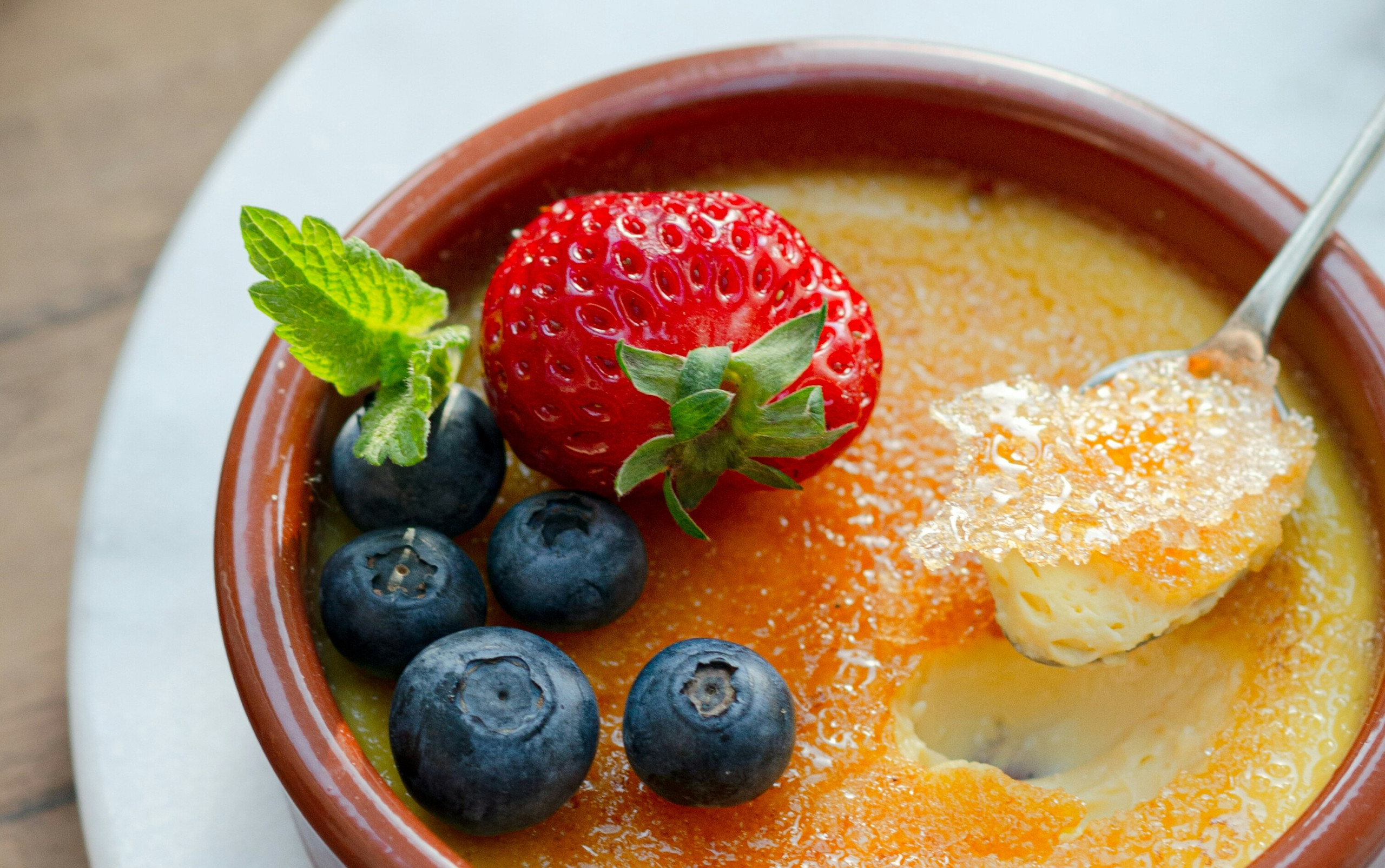 Crème brûlée mit karamellisierter Kruste, angerichtet mit Erdbeere, Blaubeeren.