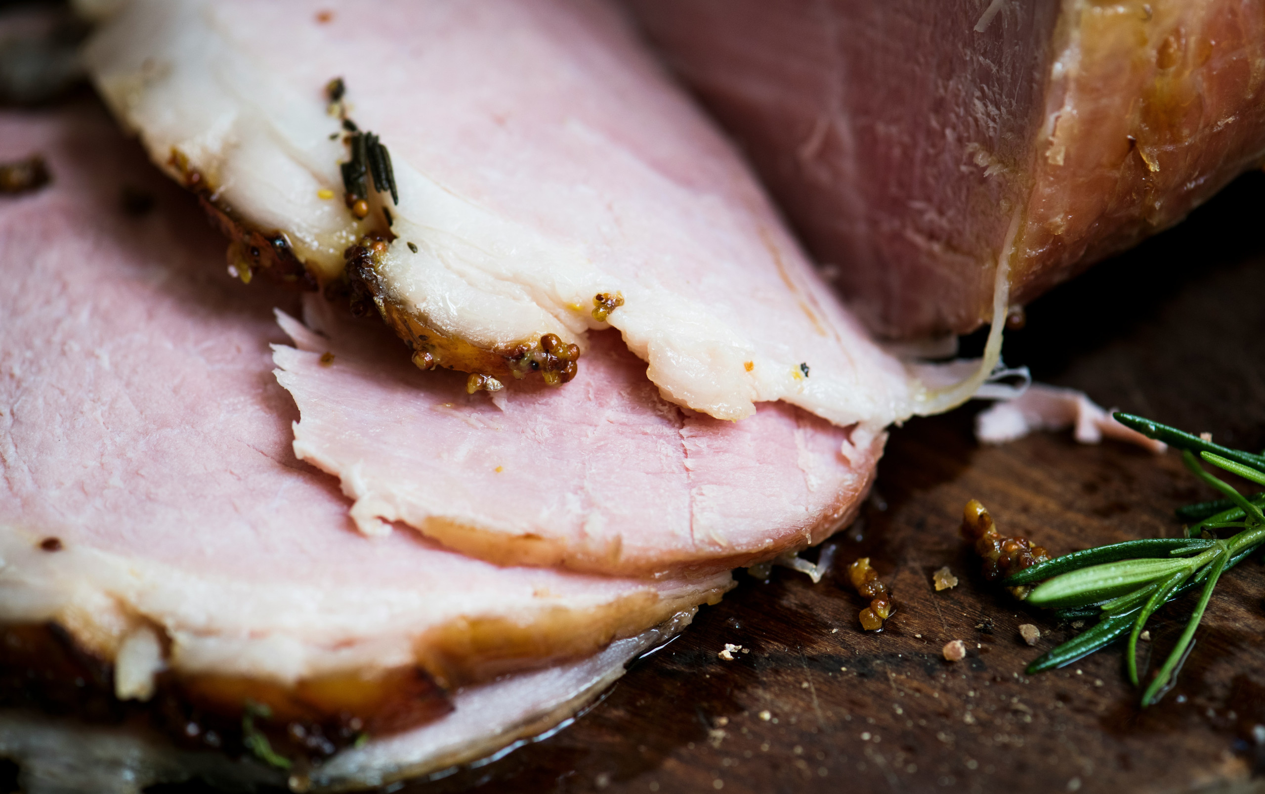 Aufgeschnittener Braten mit Kräuterkruste auf einem Holzbrett, garniert mit Rosmarin.
